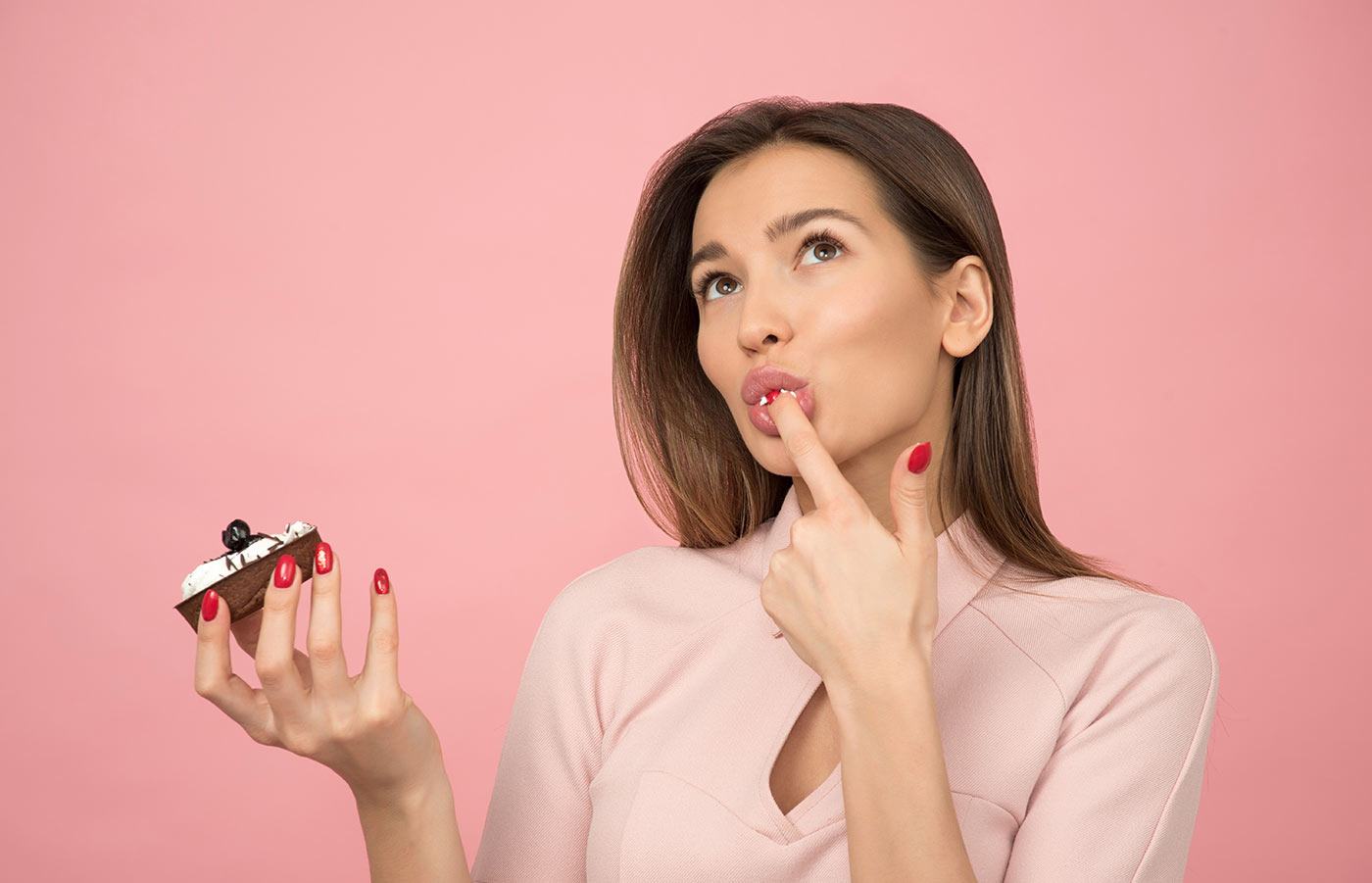 woman-eating-cupcake-while-standing-near-pink-background-1036621